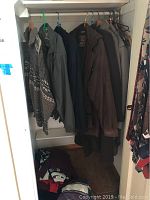 Closet view showing multiple men's sweaters and jackets hung on hangers, including patterned wool sweater and other coats in neutral colors.