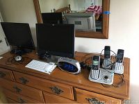 Photo of entire electronics lot on wooden dresser: includes two computer monitors, white keyboard, black mouse, digital clock, and three VTech cordless phones with base station.