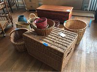 Photo showing large woven basket chest, multiple baskets including planter baskets, and two vases on wooden floor.