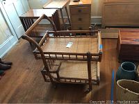 Full side view of rattan cart showing two woven shelves and vertical frame with caster wheels.