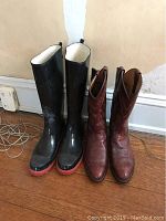 Two pairs of boots, one pair black with red soles and rubber exterior, another pair brown leather Western boots.