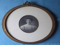 Full view of oval framed matted vintage photograph of a young lady early 1900s with decorative detail on frame top.