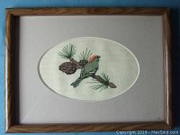 Framed cross stitch showing a bird on a pine branch with pine cones inside an oval mat and wooden frame.