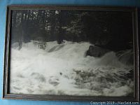 Front view of the vintage black and white photo of water falls in a wooden frame placed on a dark surface.