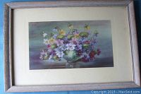 Framed watercolor painting showing a bunch of violets in a green vase with muted green and purple background, visible signature at bottom left.