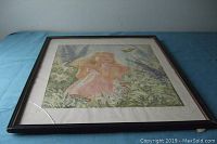 Full view of framed fabric painting showing girl with butterfly and cracked glass bottom left corner