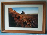 Framed photograph of mountain landscape with rocky terrain under clear sky, showing wood frame and triple-colored matting.
