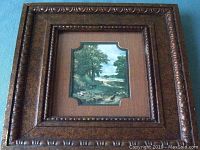 Antique wooden frame with carved details surrounding a small landscape painting showing a riverbend and trees, with a shaped inner mat window.