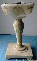 Front view of marble lamp base showing smooth polished surface, carved floral and scroll motifs on bowl section, fluted stem, and square base