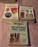 Photo showing all three Antique Trader price guide books stacked on a surface, titles and cover images visible.
