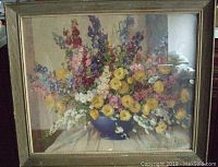 Framed artwork showing bowl of multicolored flowers under glass in a gold wood frame