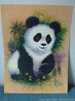 Photograph of a lithograph print depicting a baby panda bear sitting surrounded by greenery and small flowers, signed by K Chin.