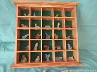 Wooden shelf with 25 compartments each holding a ceramic Whimsie animal figurine, displayed against green cloth background.