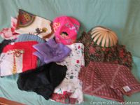 Overview of scarves and hats including pink Dora hat, striped folding beach hat, and various scarves with different color patterns laid on green background.