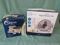 Photo showing boxed Mainstays black 9-inch high-velocity fan and boxed Cuisena microwave steam cooker.