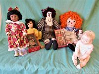 Group of six dolls including two Raggedy Ann dolls, two boxed vintage dolls, one dark-skinned doll, and one baby doll in white and blue outfit.