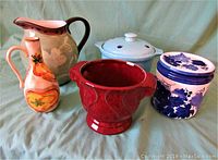 Front view showing five ceramic items: large floral pitcher, white canister with lid, blue and white grapevine patterned canister, red bowl with chip, and decorative jug.