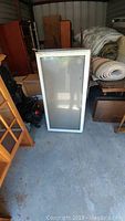 White framed window with clear glass, size approximately 16" x 36" leaning against boxes in storage.
