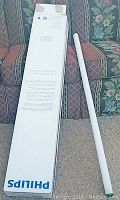 Photo showing a single white tubular fluorescent bulb beside a long box with Philips branding, the bulbs appear new and unused in original packaging.