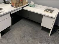 Photo showing the L-shaped white office desk with attached pedestal drawers and clear flat surface.