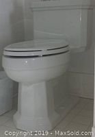 Side view of a white Kohler Kathryn one-piece toilet installed in a bathroom corner with tiled floor and walls.