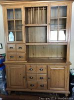 Front view of pine hutch showing glass cabinet doors on upper section, vertical slats for dish storage, multiple drawers, and lower cabinet doors.