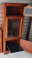 Photo showing a wood display cabinet with two glass doors open revealing shelves and storage compartments.