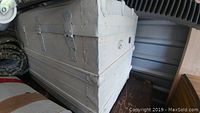 Side view of the white painted antique steamer trunk showing metal riveted edges and latches.
