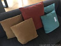 Five down filled pillows displayed on dark couch, showing mustard yellow, rust red, and teal blue covers.
