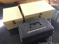 Photo showing three storage boxes: two beige photo storage boxes and one black hard plastic box labeled 'ULTIMATE'