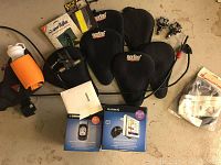 Wide view of all items included in the bike accessory lot: 2 Garmin GPS devices in boxes, Serfas seat pads, bike pedals, water bottle holder, cable, and strap