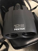 Close-up of black Pentax binoculars with 12x24 UCF magnification label visible.