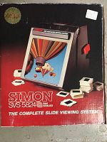 Box front showing the main image of the Simon SVS 5824 slide viewing system with a colorful hot air balloon slide inserted, several slide mounts around, and system features.