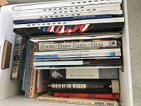 Photo showing an overhead view of a box of various books including art gallery catalogs, food and health guides, history books by David McCullough, and handwriting analysis.