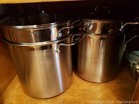 Two stacked stainless steel pots, likely the main sauce pots from each set, displayed inside a cabinet.