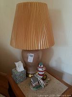 Full view of large beige lamp with pleated lampshade and part of lighthouse lamp base visible