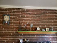 Wide view of brick wall shelf showing the clock, barometer, two metal candle holders with white taper candles, plate, two mini vases, and two carved figurines.