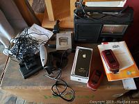 Overview showing all items in the lot including iPhone 4 in box, Nokia 6350 flip phone and manual, pedometer, portable radio, TomTom GPS device, and cables