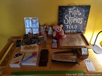 Full view of assorted items on a wooden table including figurines, prayer charms, knives, lighter, and artwork.