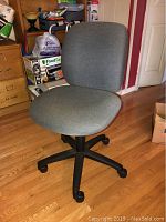 Front view of gray upholstered office chair with cushioned seat and backrest and black wheeled base.