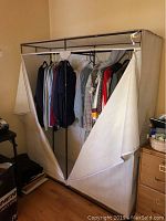 Full view of wardrobe rack with doors unzipped showing some clothes hanging inside.
