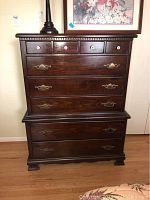 Front view showing dark wood surface, seven drawers with mixed metal and ceramic knobs, and visible scratches.