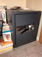 Full side view of the dark grey MEILINK ThermoSafe FS 1613 fire-safe placed against a wall with books stacked beside it.