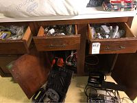 Wide view showing drawers open with plumbing parts, nuts, bolts and batteries inside drawers and on cabinet shelves. Power tools including circular saw on floor beneath cabinet.