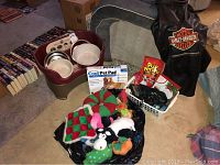 Photo showing the Neater Feeder raised feeding station with bowls, Cool Pet Pad box, assorted pet toys, and Harley-Davidson pet coat beside a large soft-sided pet bed.