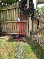 Soaker hose, tomato cages and red trellis hanging on wooden fence near garden area.