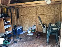 Wide view of shed interior showing stacked green plastic chairs, shelving with various tools and items, blue cooler, garden supplies, and floor jack.