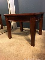 Side view of one dark wood end table showing leg design and wood joinery.