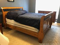 Full view of pine wood sleigh bed frame with black comforter