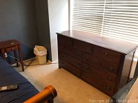 Dark wood nine drawer dresser against wall under window, showing front and top surfaces.